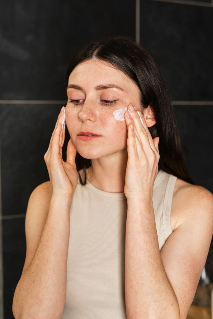 Young brunette applies sunscreen to her face. Skincare routine. Concept of skincare.